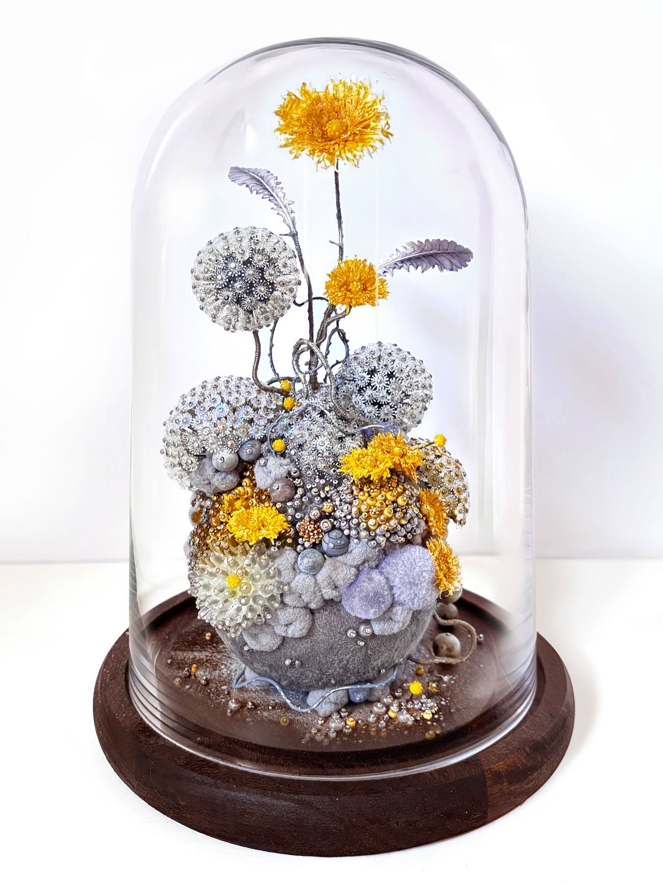 An intricate sculpture inside of a glass dome vitrine by Amy Gross of imaginative flora made from paper and beads