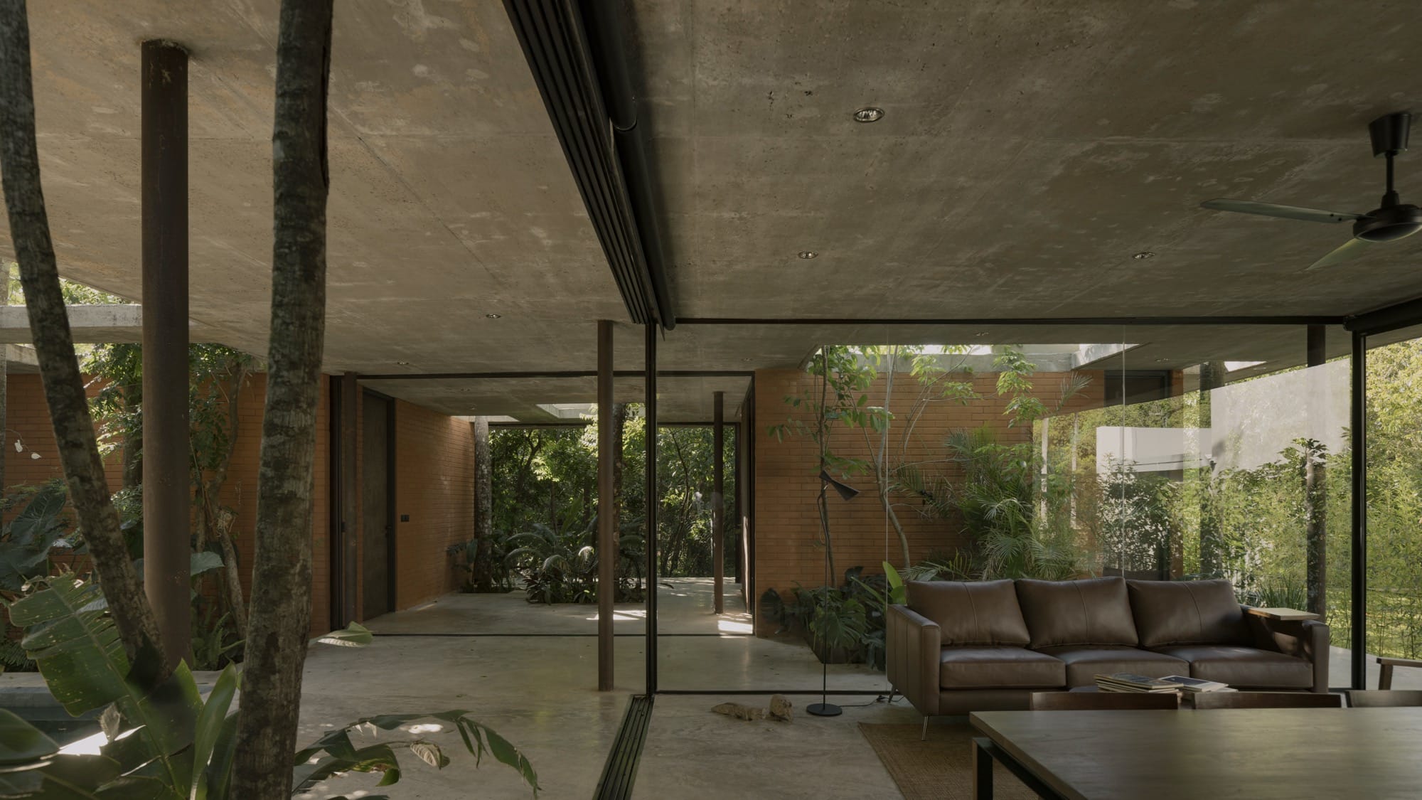 The interior of a contemporary concrete, glass, and steel home amid trees and tropical plants