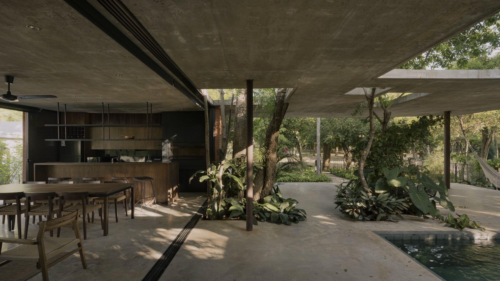 The interior of a contemporary concrete, glass, and steel home amid trees and tropical plants