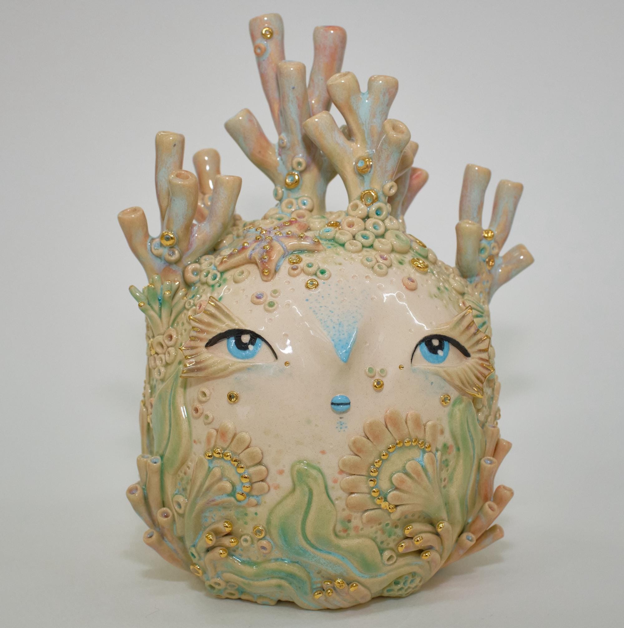 a ceramic sculpture by Abi Castillo of a head with corals protruding from the top of its head and sides, surrounded by small barnacle, seaweed, and bubble details