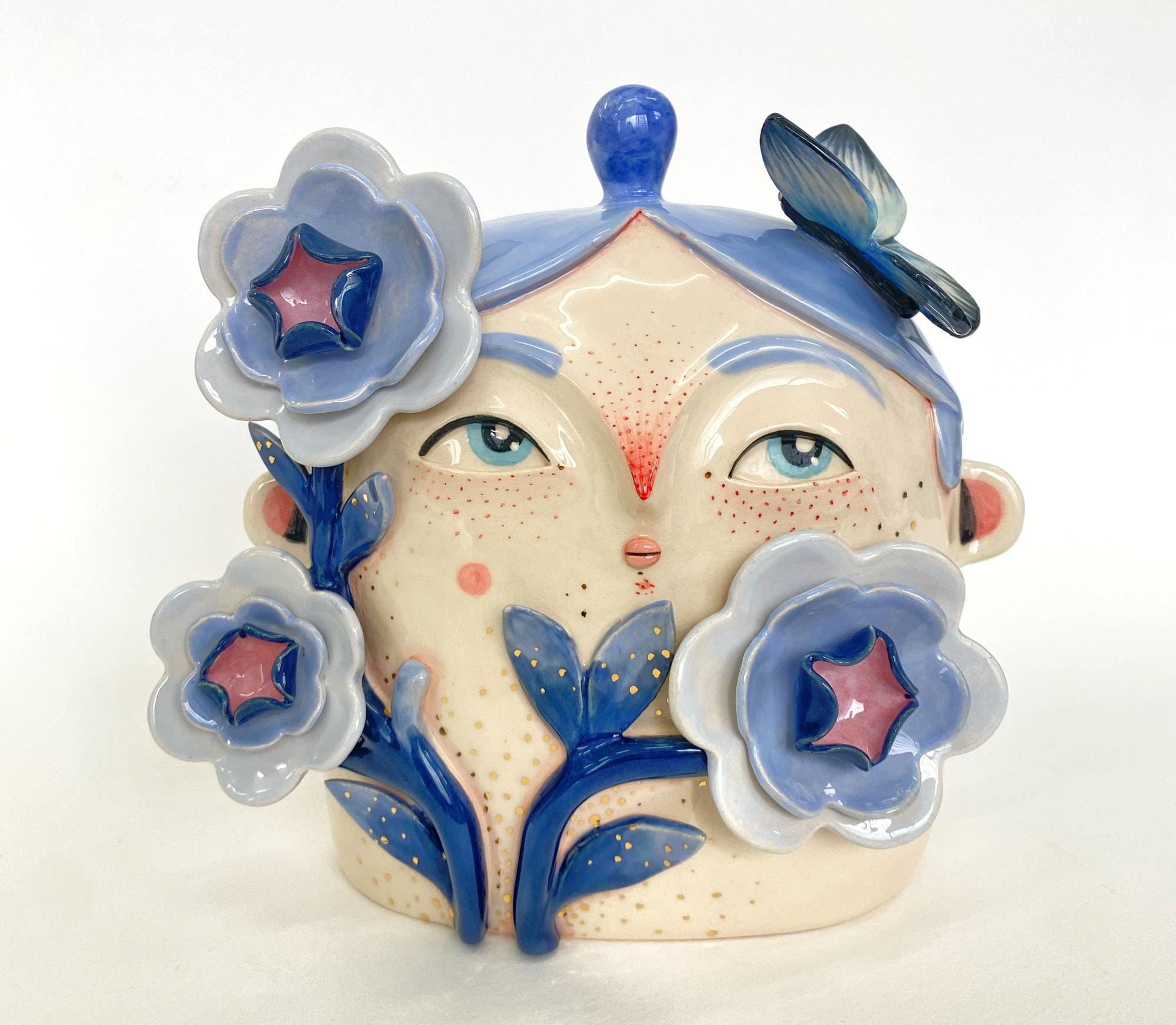 a ceramic sculpture by Abi Castillo of a head with blue hair, framed with blue flowers and butterflies