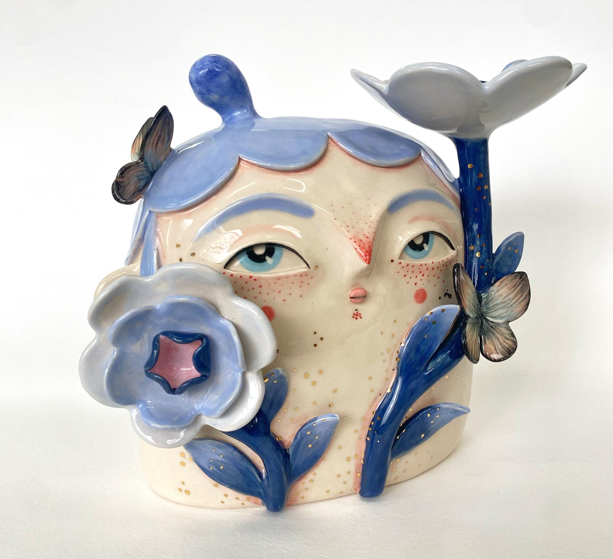 a ceramic sculpture by Abi Castillo of a head with blue hair, framed with blue flowers and butterflies