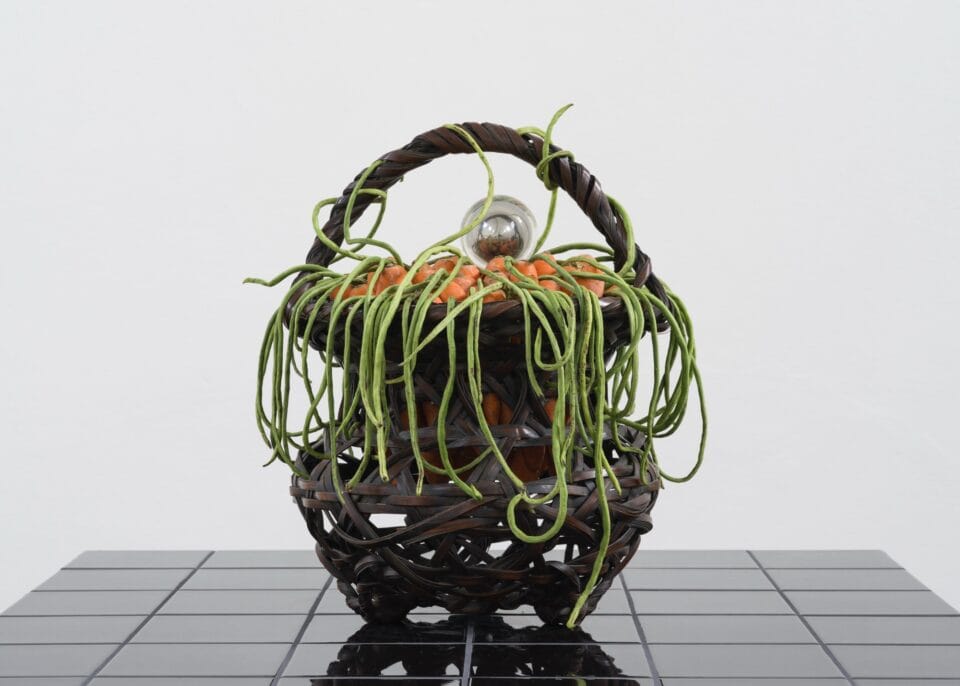 green fronds hang over a basket with orange flowers in the center