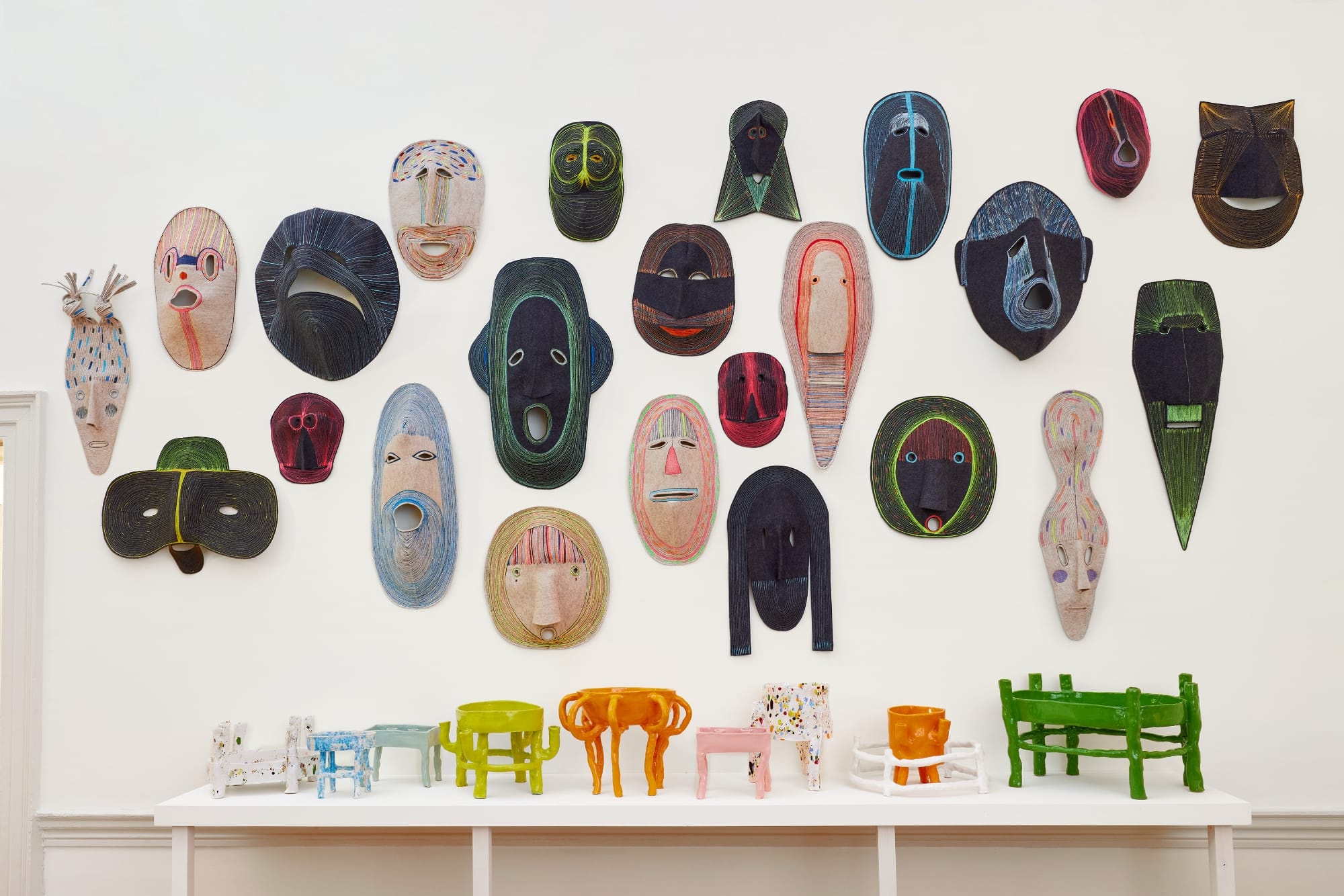 a collection of textile masks on a wall above colorful ceramics