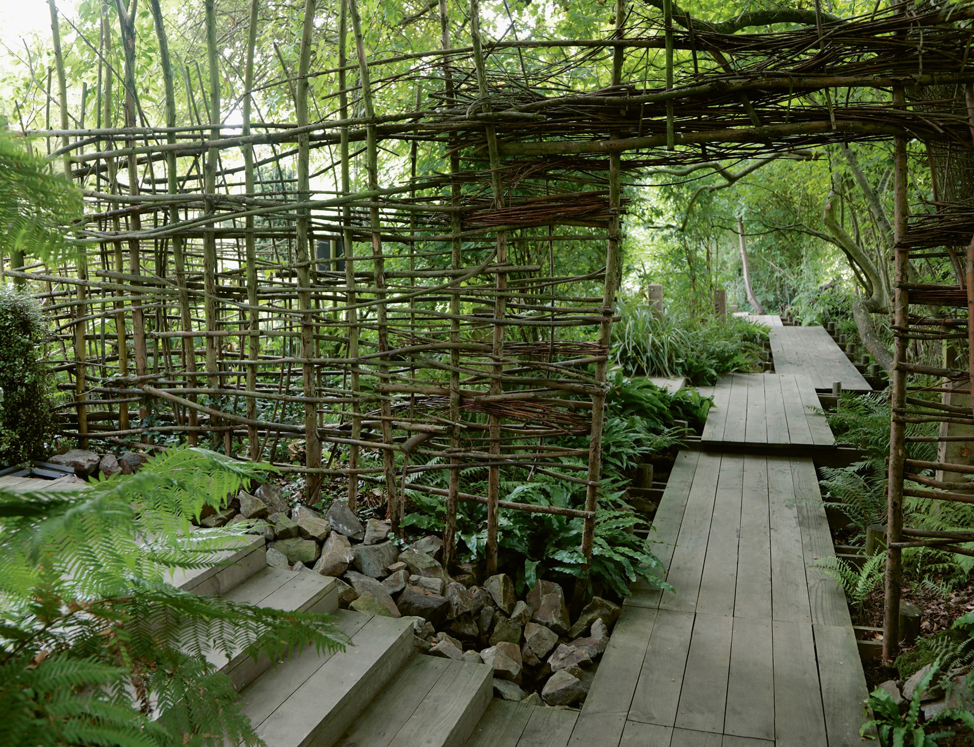 a wood walkway through a green forest with scaffolding made of branches
